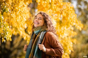 Joyful woman in a scarf and coat standing outside in the fall