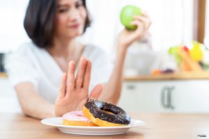 Woman holding an apple and pushing away a plate of donuts