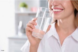 Woman smiling and holding a glass of water to her lips