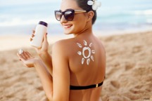 Woman smiling on the beach with a sun drawn on her back in sunscreen
