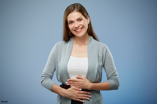 brunette woman smiling, holding stomach