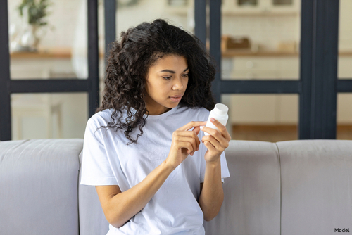 Woman sitting on a couch reading the info on a pill bottle