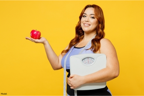 Confident woman in activewear holding an apple and a weight scale