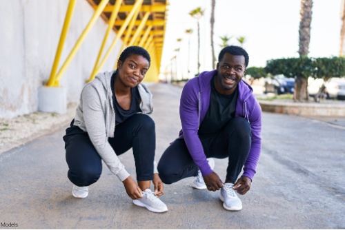 Man and woman outdoors in activewear stopping to tie their shoes