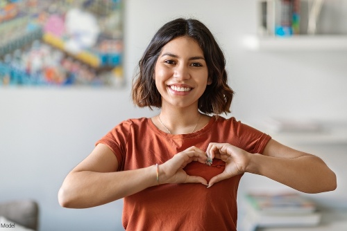 Confident woman with short brown hair smiling and holding her hands in a heart shape over her chest