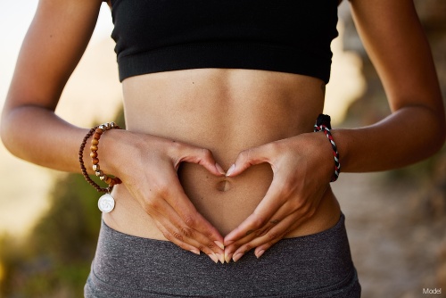 Woman holding her hands in the shape of a heart around her belly button